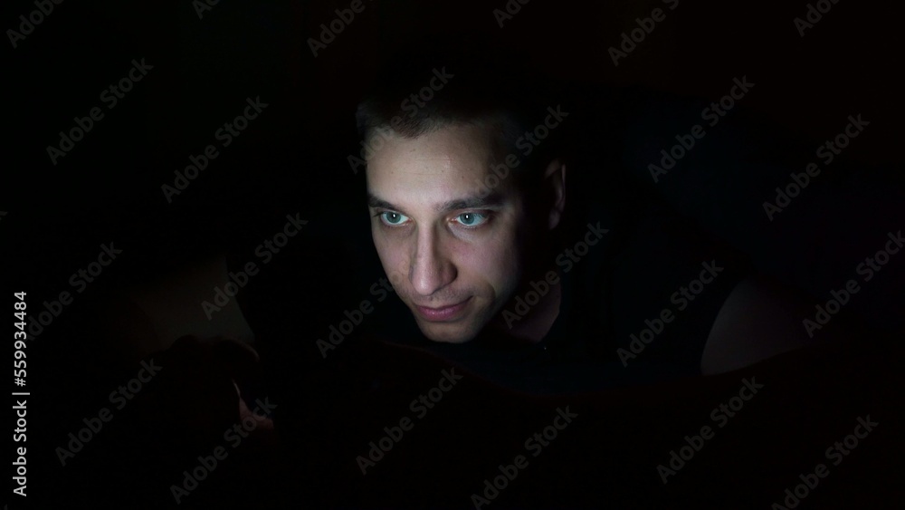 young guy looks at the phone before going to bed at night. Examines information on the phone. young guy looks at the phone before going to bed at night. Examines information on the phone.