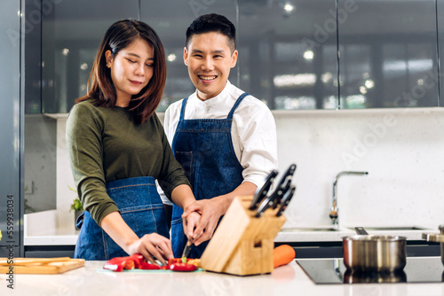 Young asian family couple having fun cooking together and preparing salad with cook food on counter standing on table.Happy couple looking to preparing food in kitchen.