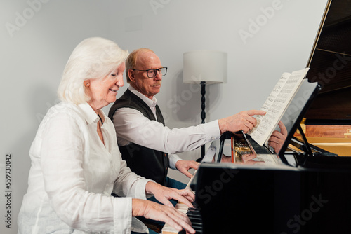 Older couple studying piano together and reading music sheet