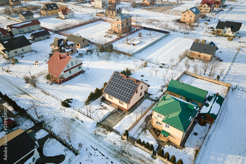 Aerial view of house roof with solar panels covered with snow melting down in winter end for producing clean energy. Concept of low effectivity of renewable electricity in northern region