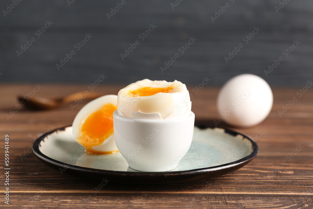 Plate with soft boiled egg on wooden table against black background Plate with soft boiled egg on wooden table against black background