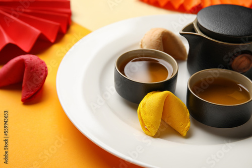 Plate with fortune cookies, teapot and cups on color background, closeup. Chinese New Year celebration