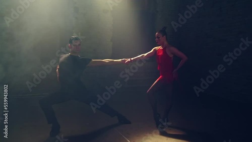 Front view ballroom dancers dancing passionate tango eye to eye, approaching each other, man takes woman by hand, lunges, presses her to him, she makes foot swing to side. Loft atmosphere,stage smoke. photo