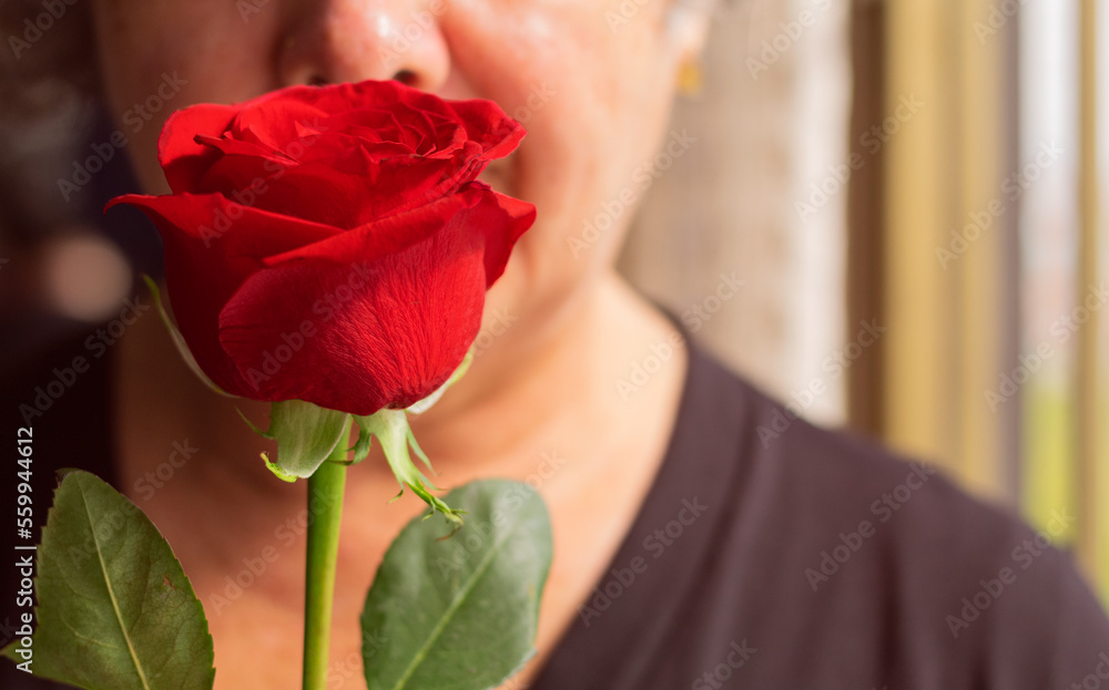 A woman holding a red rose close to her face.
