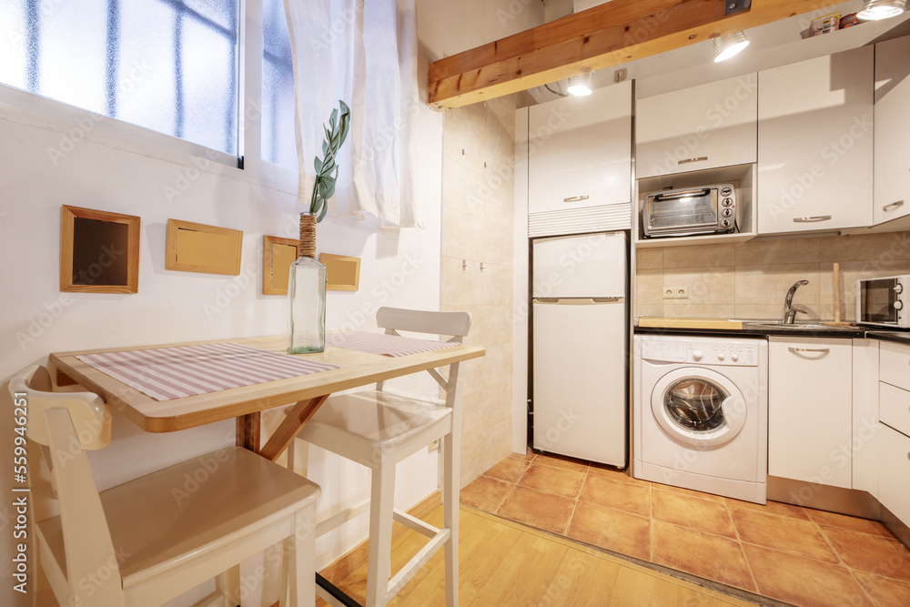 Cozy studio apartment for vacation rental with kitchen open to living room with conventional design furniture with white furniture and black countertops and folding wooden table Cozy studio apartment for vacation rental with kitchen open to living room with conventional design furniture with white furniture and black countertops and folding wooden table