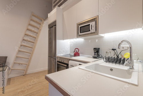 Studio apartment with open kitchen with white cabinets  wooden staircase and stainless steel appliances