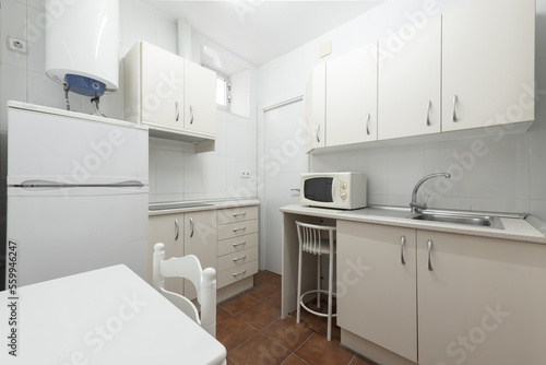 Small kitchen with white cabinets, appliances of the same color, an electric water heater and a white wooden folding kitchen table
