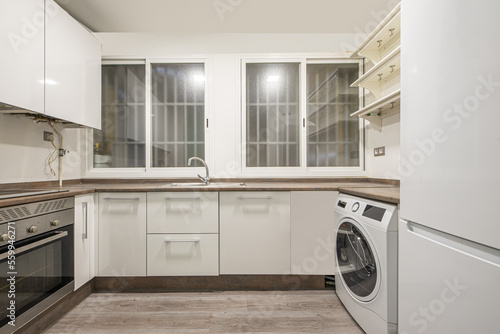 kitchen with white cabinets, brownstone worktops, twin barred windows and a white washing machine and fridge