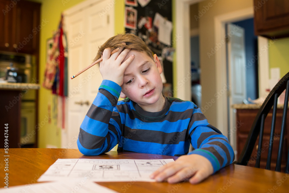 Young Boy Holding a Pencil Does Homework at Kitchen Table Young Boy Holding a Pencil Does Homework at Kitchen Table