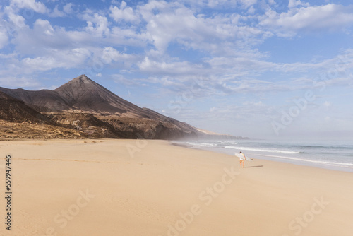 Surfer on otherwise empty beach with rock formation in background, Fuerteventura, Canary Islands, Spain photo