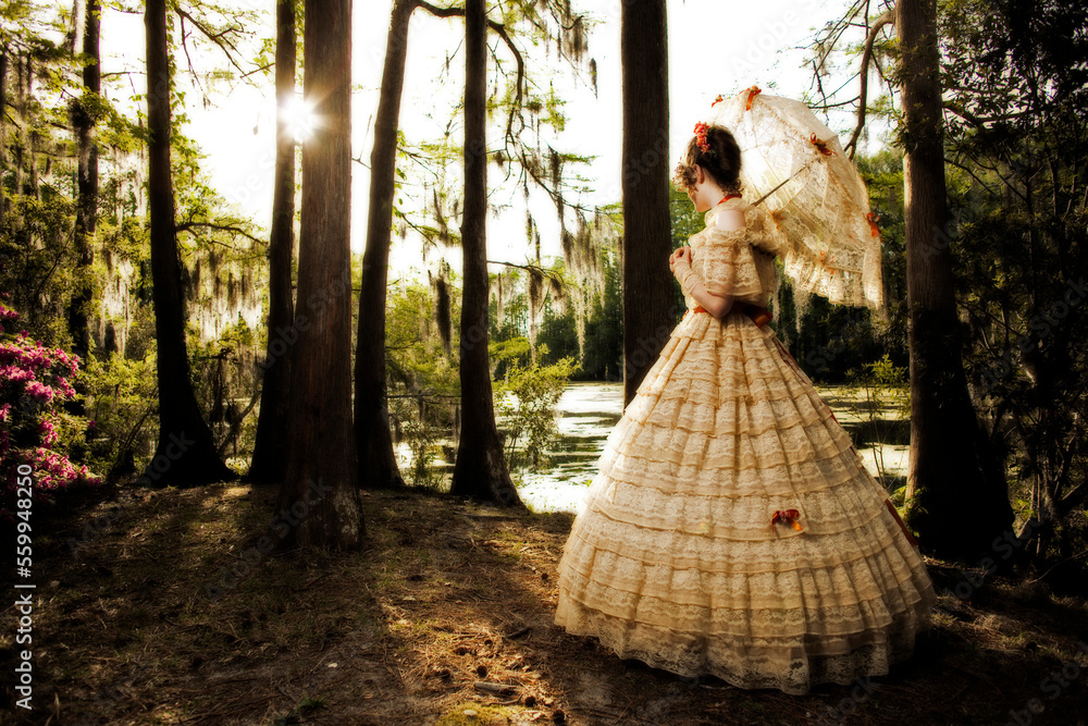 A young woman poses in a Southern Belle outfit , including a large, ornate period-dress and parasol, near a lake.