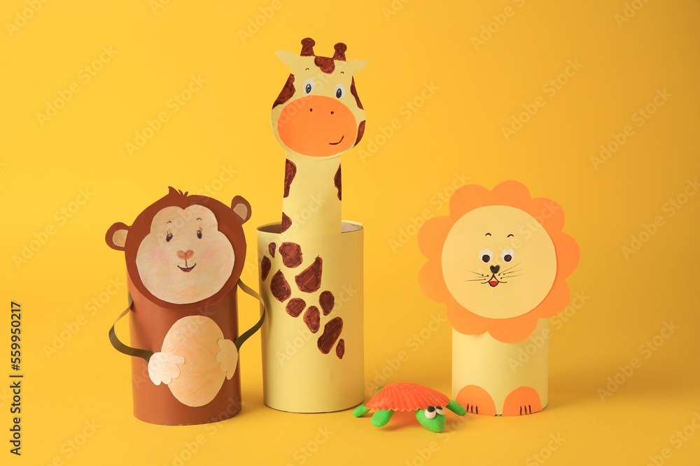 Fototapeta premium Toy monkey, giraffe and lion made from toilet paper hubs with plasticine turtle on yellow background. Children's handmade ideas