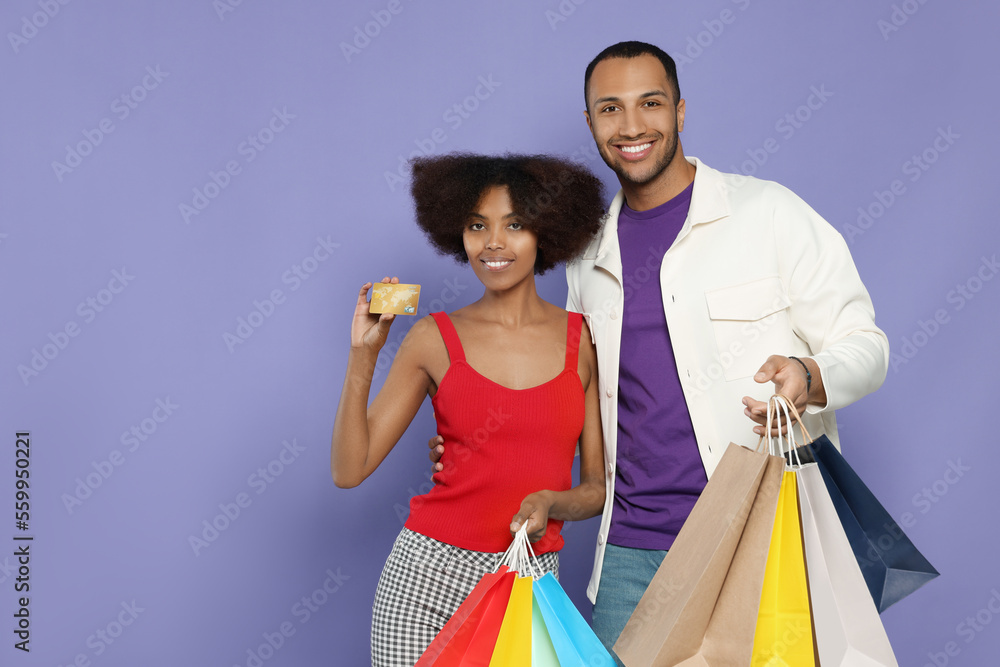 Happy African American couple with shopping bags and credit card on purple background. Space for text Happy African American couple with shopping bags and credit card on purple background. Space for text