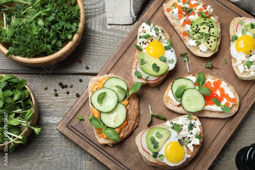 Different delicious sandwiches with microgreens on wooden table, flat lay