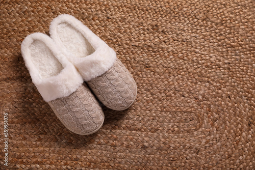 Pair of warm stylish slippers on wicker carpet, top view. Space for text