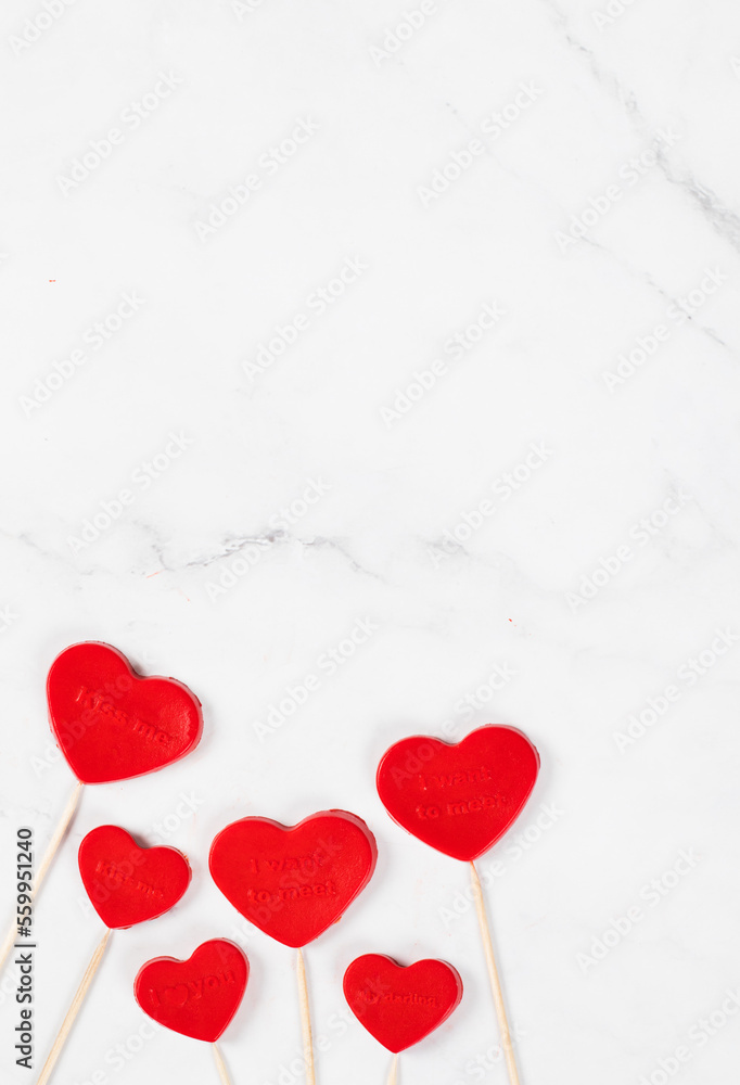 Vegan dessert.  Creamy jelly sweets candies in the shape of a red heart with thematic inscription, on a wooden sticks. Valentine's Day. White background. Copy space. Top view