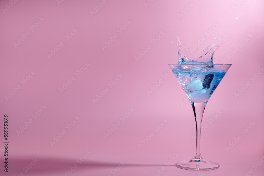 Cocktail splashing out of martini glass on pink background, space for