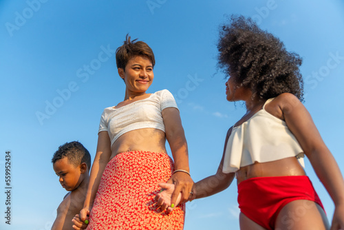 Happy African family on summer holiday vacation. Mother holding hands with little daughter and son walking together on the beach at sunset. Parents with kid enjoy outdoor lifestyle together at the sea
