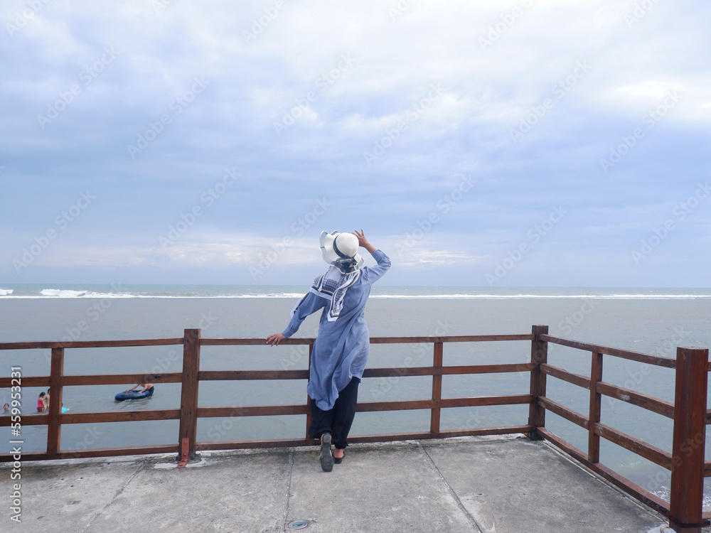Back of the woman in the hat on the tropical beach who is looking up at the sky and the sea
Back of the woman in the hat on the tropical beach who is looking up at the sky and the sea