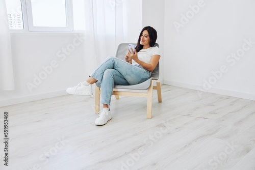 Woman sitting on chair with phone in hand in new apartment, online shopping via phone, online shopping
