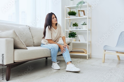 Woman sitting on the couch at home leg and foot pain, sprain and muscle strain, leg injury