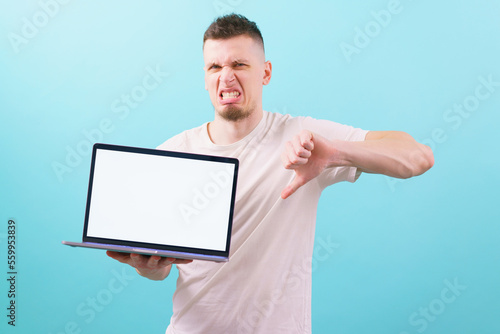 A man holding a laptop with an empty blank screen and shows thumb down on blue background. White. Guy. Business. Holding. Display. Device. Caucasian. Digital. Expression. Work. Internet