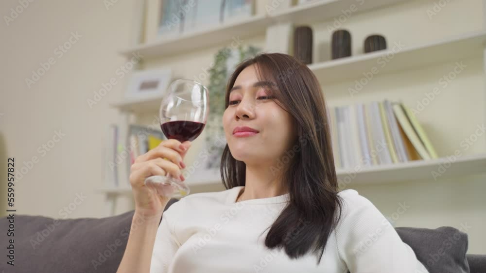 Asian beautiful woman drink wine while sitting on sofa in living room. Asian beautiful woman drink wine while sitting on sofa in living room.