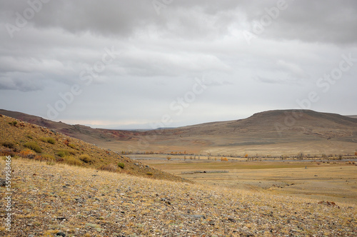 Endless autumn steppe surrounded by hills under a cloudy cloudy sky.