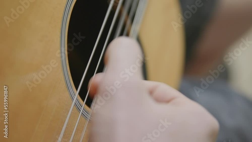 Slow motion footage of a thumb strumming on the strings of a guitar.