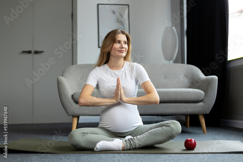 Young beautiful pregnant woman exercising, meditating, doing yoga sitting in lotus pose. Pregnancy yoga and fitness concept 