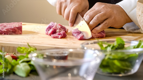 Chef butcher expertly wields his sharp knife, deftly slicing through the raw meat, the muscles rippling beneath his sleeves as he carefully portions out the cuts.