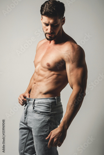 Male model with perfect body in jeans posing over grey background. Close-up. Studio shot.