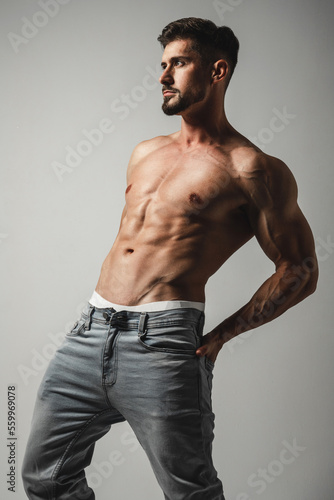 Male model with perfect body in jeans posing over grey background. Close-up. Studio shot.