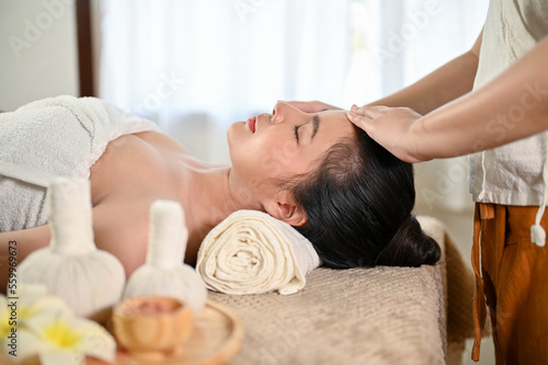 Calm and peaceful Asian woman getting facial treatment massage by a professional masseur
