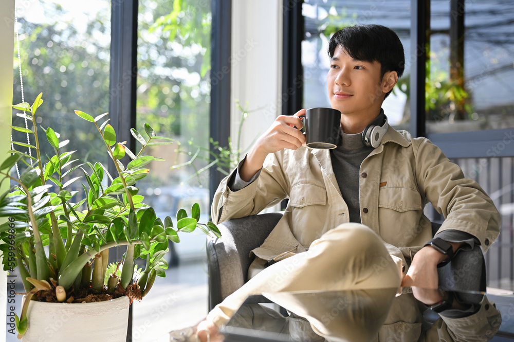 Fototapeta premium Successful Asian male enjoys having morning coffee at the coffee shop, daydreaming