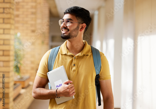 University student, college and indian man with a tablet and backpack while walking down campus corridor. Young gen z male happy about education, learning and future after studying at school building photo
