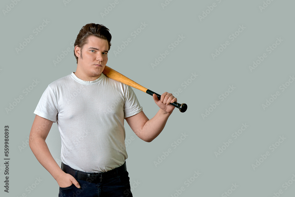 A stylish man holds a bat on his shoulder on a gray isolated background A stylish man holds a bat on his shoulder on a gray isolated background