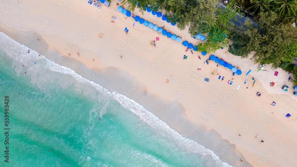 Aerial tropical landscape of Kata Beach with blue beach umbrellas and tourists along the beach. Drone view over the coastline of Phuket, a famous travel destination in the South of Thailand.