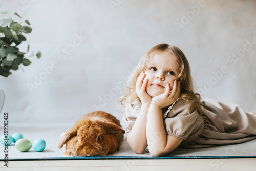 little blonde girl in vintage dress near retro background and vase with green branches eucalyptus gum tree, brown bunny rabbit spring day, happy childhood, simple and cozy life, happy Easter eggs hunt