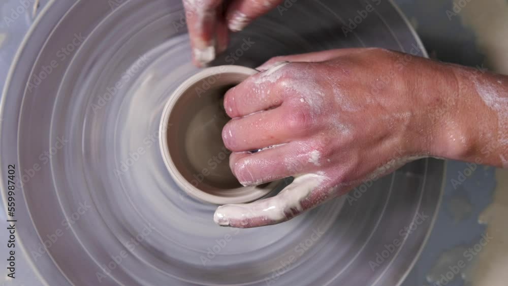 Top view of a female potter working on a potter's wheel. The master is shaping a mug of white clay. Close-up. Slow motion Top view of a female potter working on a potter's wheel. The master is shaping a mug of white clay. Close-up. Slow motion