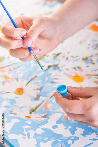 A hand with brush drawing picture of flowers with acrylic paints on canvas. Art concept.