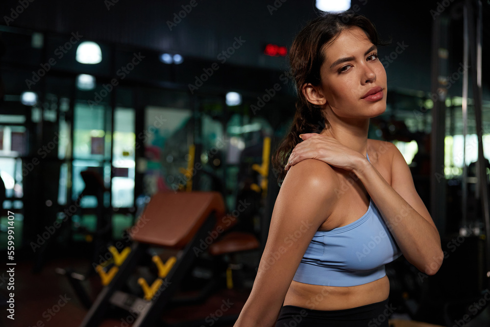 young sporty woman feeling tired and shoulder pain from workout in the gym