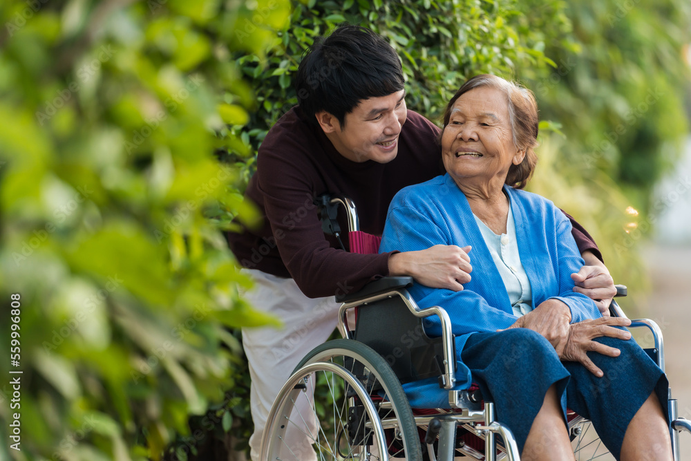 happy young man (grandson) embracing with senior woman in wheelchair at park happy young man (grandson) embracing with senior woman in wheelchair at park