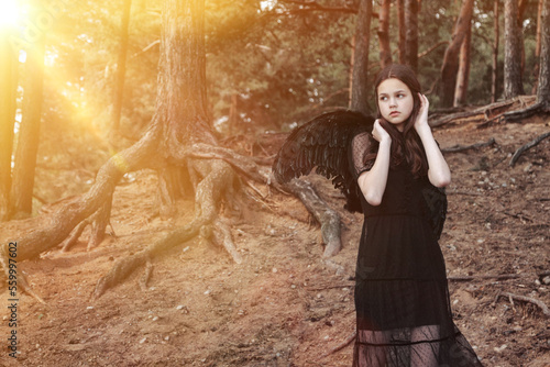 Teen girl with long hair in black wings posing in fairy tale forest. Young pretty lady Princess angel at mysterious woodland. Vintage retro image, fantasy concept. Copy space for advertising text