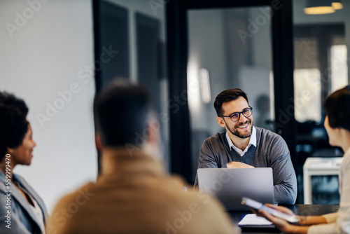 A happy businessman is sitting in the co working space with colleagues and having briefing.