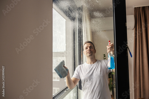 A man is spraying glass solution on a window and cleaning it.
