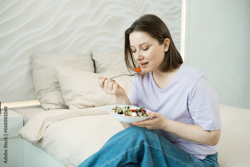 adult oversized woman sitting on bed and eating fresh vegetable salad adult oversized woman sitting on bed and eating fresh vegetable salad