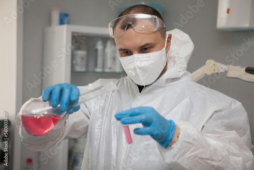 Scientific virologist. Biologist in protective suit and blue gloves holds test tube and flask. Test tube with viruses concept. Medicine and antidote in doctor hands. Virus University employee.