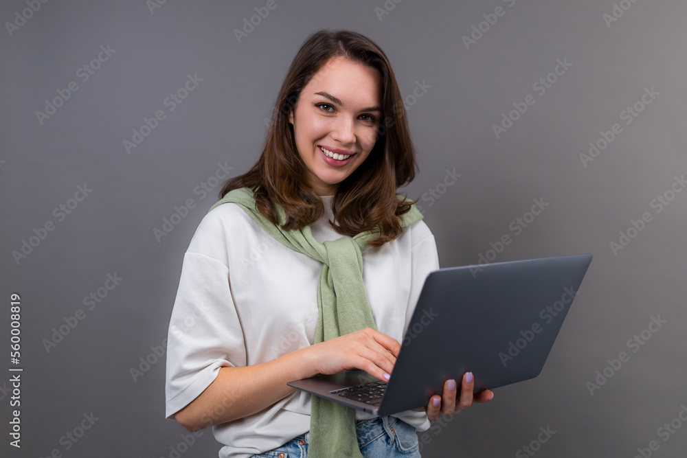 Fototapeta premium A smiling young woman with a laptop looks into the camera. Student with a laptop, gadgets for study and work