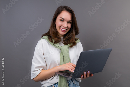 A smiling young woman with a laptop looks into the camera. Student with a laptop, gadgets for study and work